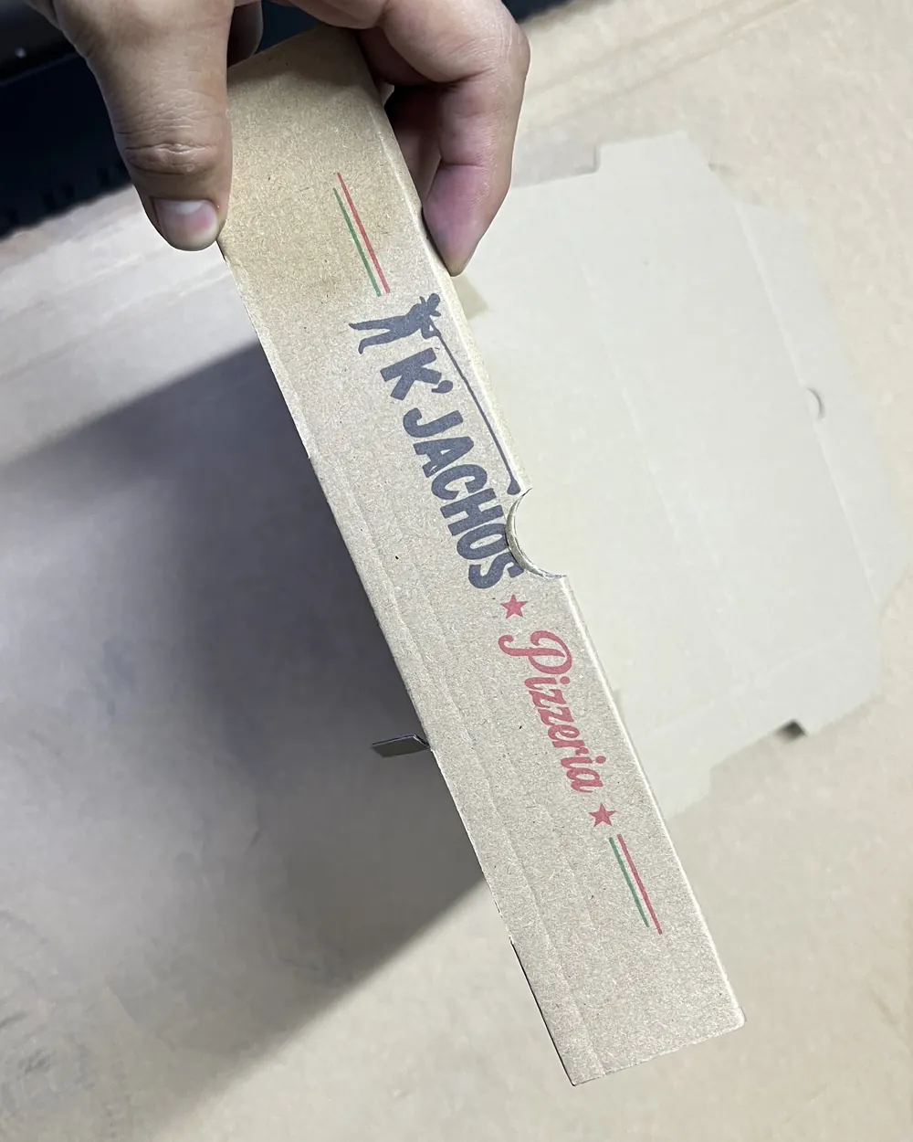 Mano que sostiene una plancha de caja doblada con el costado impreso a color